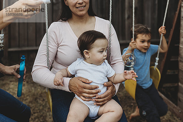 8 Monate altes Baby auf Schaukel mit Mutter  die aufmerksam auf die Blase schaut