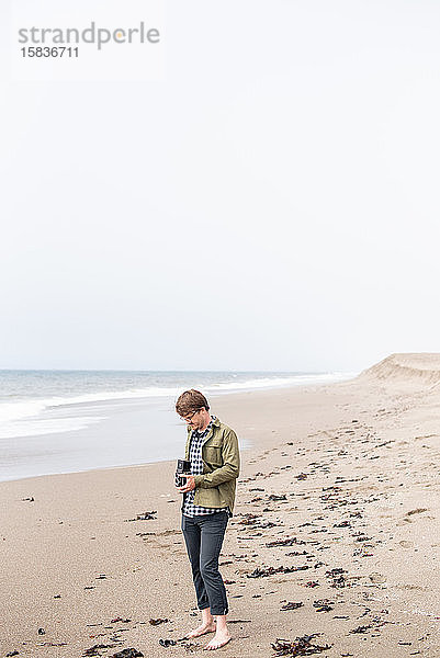 Junger Mann steht am Strand und fotografiert mit einer Filmkamera