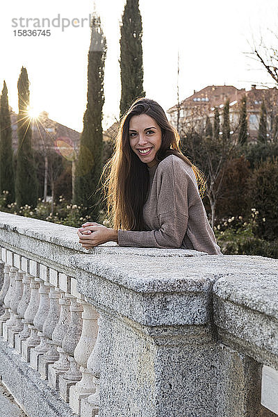 Lächelnde junge Frau  die auf einer Steinbrücke lehnt