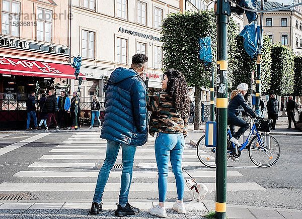 Freundin und Freund warten an einer Ampel und unterhalten sich in Europa