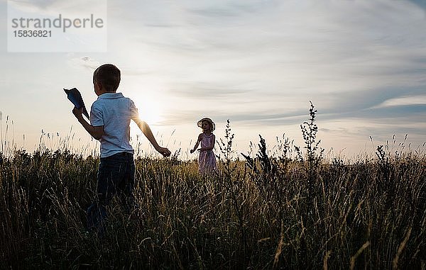 Geschwister spielen draußen bei Sonnenuntergang mit Papierfliegern zusammen