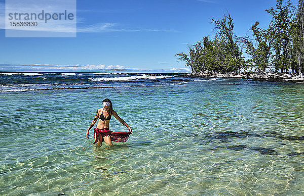 Eine junge Frau verlässt eine seichte Lagune in der Nähe von Makalawena Beach