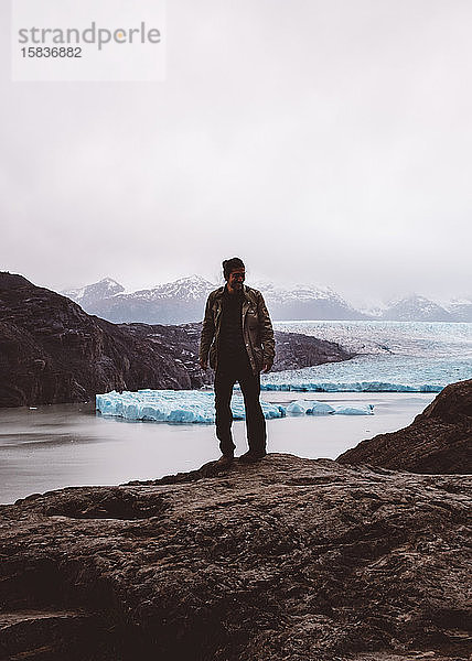 Mann steht lächelnd auf Felsen am See mit Gletschern