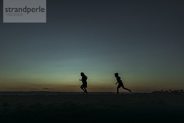 Sihouette von Bruder und Schwester rennen in der Abenddämmerung auf den Ozean zu