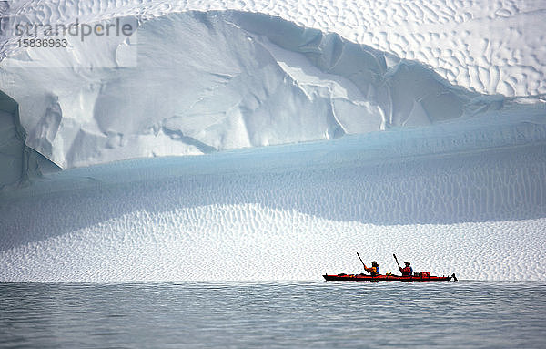 zwei Männer rudern mit ihrem Seekajak auf einem Eisberg in Grönland