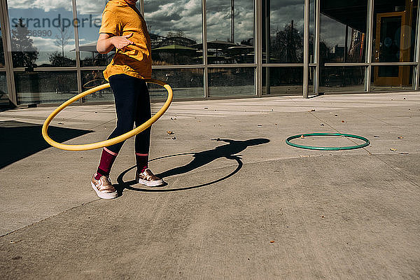 junges Mädchen  das an einem sonnigen Tag versucht  auf einer Terrasse Hula-Hoop-Reifen zu tanzen