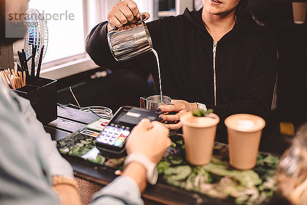 Kunde im Gespräch mit weiblichem Barista beim Kaffeekauf im Café