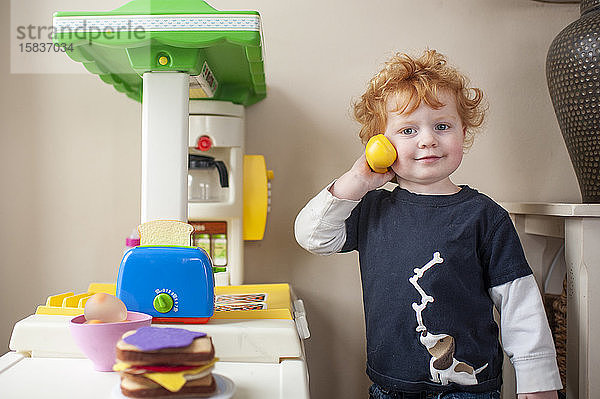 Kleinkind Junge schaut  während er in der Spielküche zu Hause ans Telefon geht