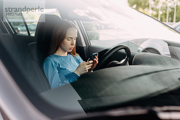 Seriöse Frau hält ihr Smartphone in der Hand  während sie im Auto sitzt.