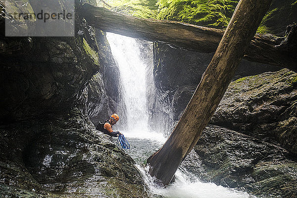 Mann wickelt Seil  nachdem er sich von einem Wasserfall abgeseilt hat.