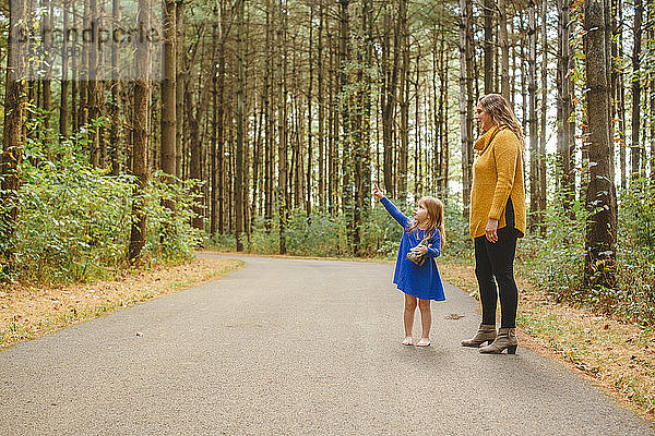 Ein kleines Kind steht auf einem bewaldeten Pfad mit der Mutter nach oben zeigend