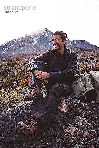 Glücklicher Wanderer sitzt auf Stein in den Bergen