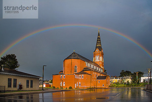 Regenbogen am Himmel über warm beleuchteter katholischer Kirche nach Regenschauern
