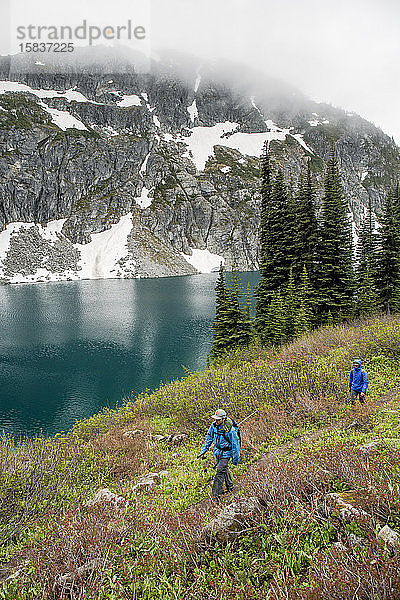 Ein Mann und eine Frau wandern an einem wolkenverhangenen  regnerischen Sommertag in den Coast Mountains um Pemberton  British Columbia  um einen wunderschönen Alpensee herum.