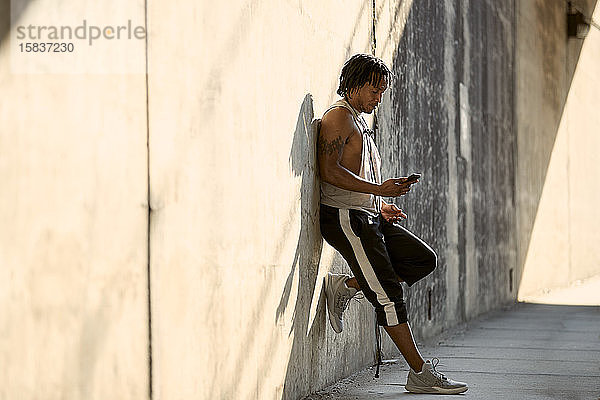 Afroamerikanischer Mann mit Blick auf Telefon auf dem Bürgersteig