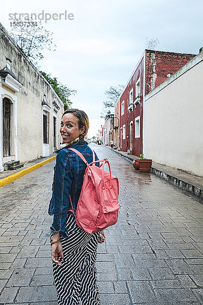 Fröhlicher Reisender mit rosa Rucksack lächelt auf regnerischen Straßen