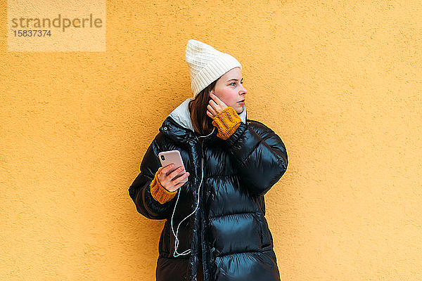 Junge Frau benutzt Smartphone  während sie an gelber Wand steht