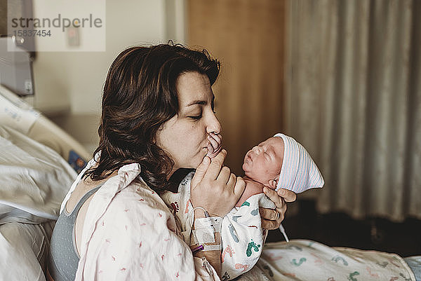 Neue Mutter im Krankenhaus küsst neugeborenen Sohn Hand
