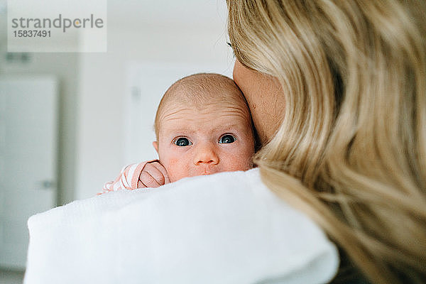 Blick über die Schulter eines neugeborenen Mädchens  das von seiner Mutter gehalten wird