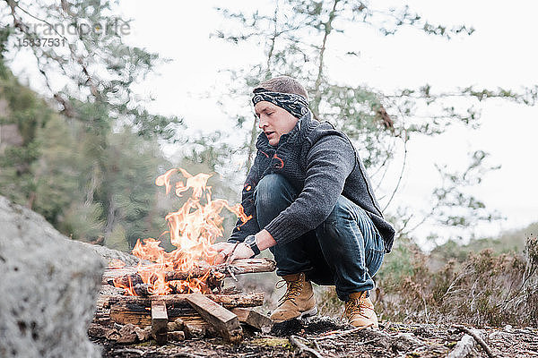 Mann legt in Schweden Stöcke an ein Lagerfeuer im Freien