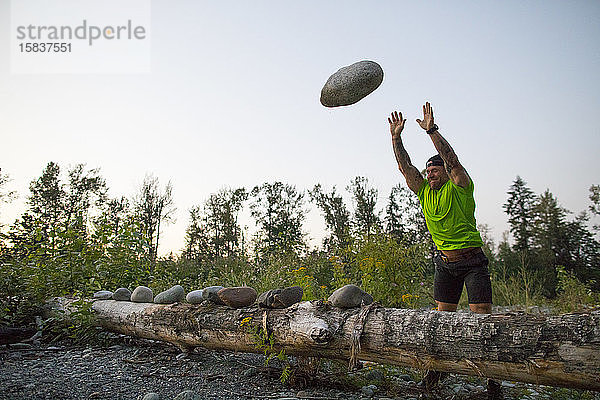 Starker Mann wirft großen Stein während eines Trainings im Freien.