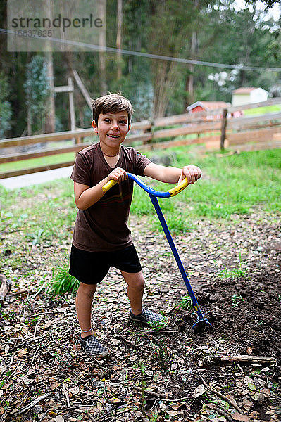 Junge lächelt im Hof  während er den Boden für einen Garten bearbeitet