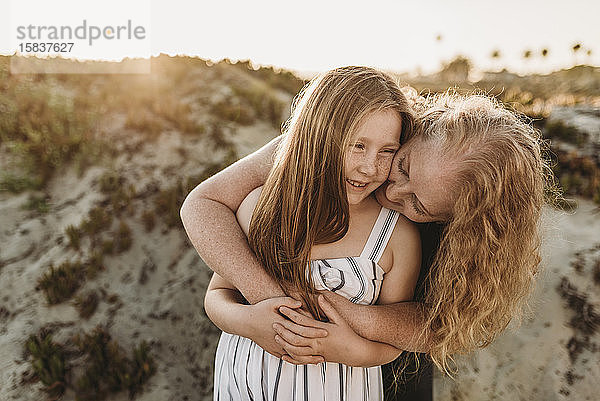 Frontansicht einer Mutter  die ihre kleine Tochter bei Sonnenuntergang am Strand umarmt