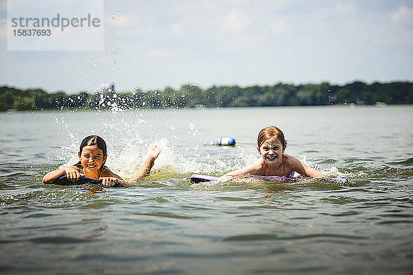 Zwei junge Mädchen in Badeanzügen auf Kickboards in einem See