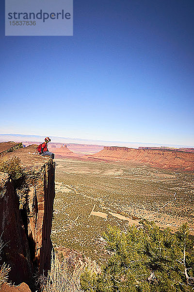 Ein Mann sitzt am Rande einer großen Klippe mit Blick auf das Monument Valley.