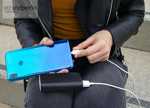 Frau  die das Handy mit einer Powerbank verbindet.