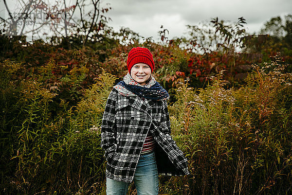 Teenager-Mädchen mit rotem Hut steht lächelnd auf einem herbstlich gefärbten Feld