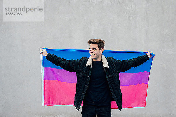 Junger Mann mit der Flagge der Bisexuellen auf grauem Hintergrund