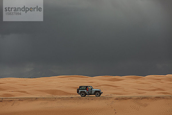Frau und ihr Jeep beim Fahren über Sanddünen unter stürmischem Himmel