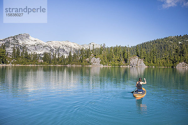Attraktive Frau paddelt stehendes Paddelbrett auf blauem See.