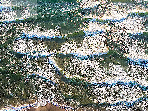 Luftaufnahme der am Strand brechenden Meereswellen.