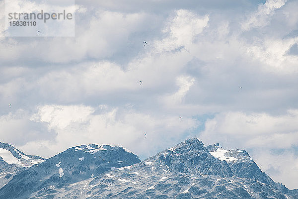 Gleitschirmflieger fliegen an einem sonnigen Tag hoch über schneebedeckten Bergen.