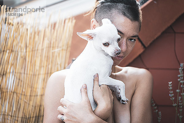 bezauberndes Porträt einer starken Frau  die ihren Hund auf dem Balkon nahe am Gesicht kuschelt