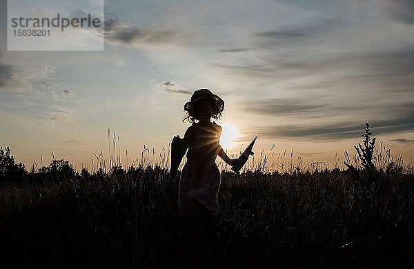 Silhouette eines Mädchens  das im Sommer bei Sonnenuntergang auf einer Wiese läuft