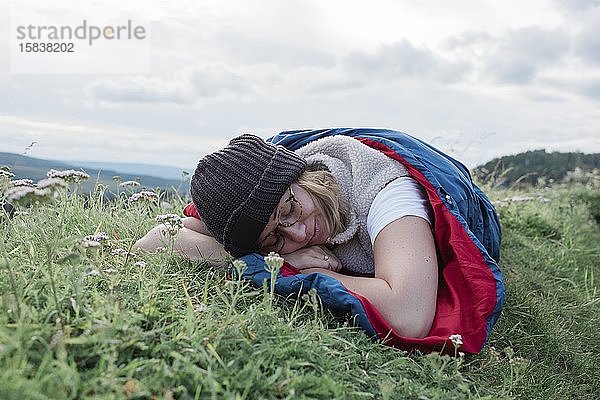 Frau schläft in ihrem Schlafsack auf einem Berg im Freien