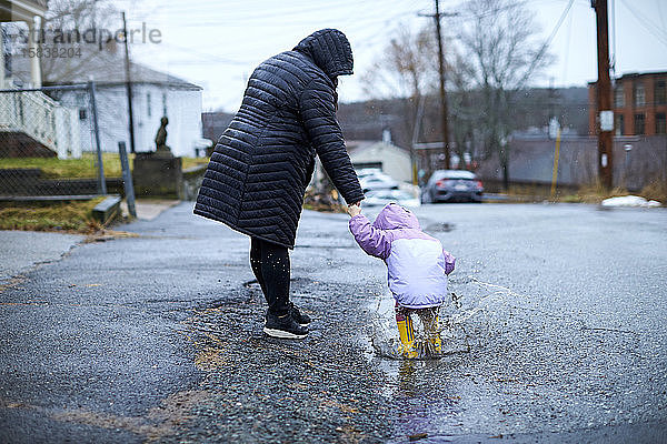 Eine Mutter und ihr Kind haben Spaß daran  an einem regnerischen Tag in Pfützen zu planschen.