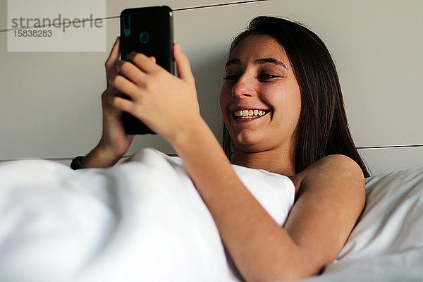 Ein junges und hübsches Mädchen ist gerade mit dem Handy im Bett aufgewacht.