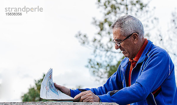Älterer Mann liest Zeitung im Park  Seitenansicht