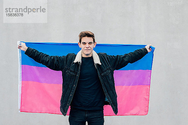 Junger Mann mit der Flagge der Bisexuellen auf grauem Hintergrund