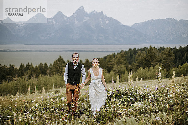 fröhlich lächelndes Brautpaar spaziert durch ein Feld von Wildblumen in Tetons