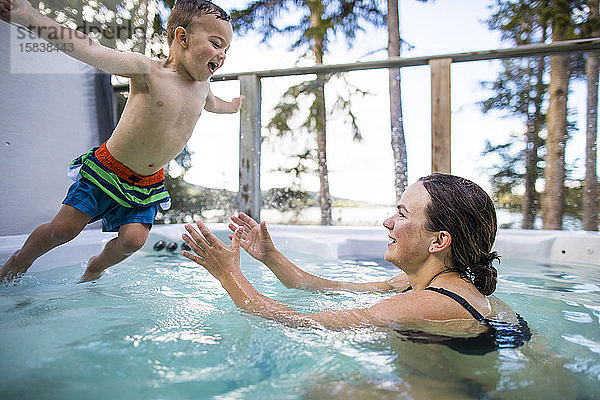 Junge springt in den Swimmingpool  die Mutter wartet darauf  ihn aufzufangen.