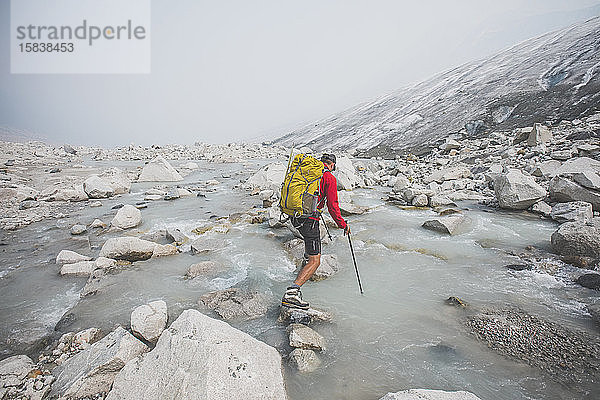 Backpacker benutzt große Felsblöcke  um den Fluss neben dem Gletscher zu überqueren.