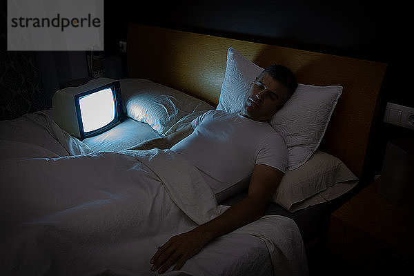 Ein Mann schläft nachts im Bett mit dem Fernseher ohne Signal. Oldtimer-Fernseher