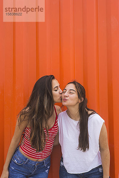 Beste Freunde küssen sich gegen orangefarbene Wand