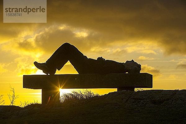 Ein Spaziergänger entspannt sich bei Sonnenuntergang auf dem Orrest Head oberhalb von Windermere  Lake District  Großbritannien.