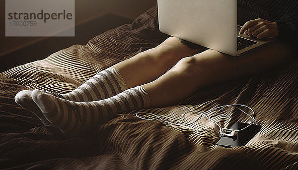 Hübsches junges Mädchen auf dem Bett liegend mit Laptop auf den Knien  Wintersocken tragend. Winter  gemütlich  Kleidung und Lifestyle-Konzept.